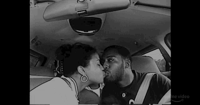 a black and white photo of a man and woman kissing in the back seat of a car .