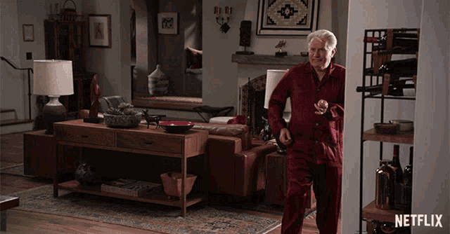 a man in a red pajama is standing in a living room with a netflix logo on the wall
