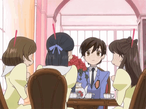 a group of girls are sitting around a table with a boy in a suit