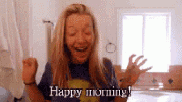 a woman is laughing and saying `` happy morning '' while standing in front of a window .