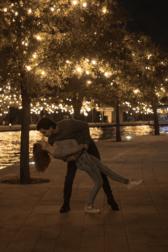 a man is holding a woman in his arms in front of a lake