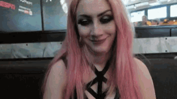a woman with pink hair and black makeup is smiling while sitting at a table .