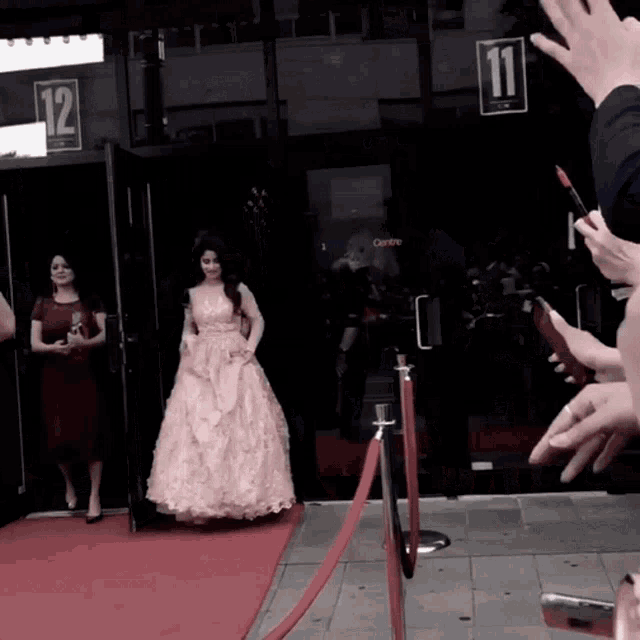 a woman in a pink dress is walking on a red carpet in front of a building with the number 12 on it