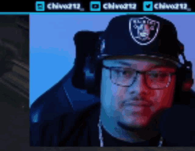 a man wearing headphones and a raiders hat looks at the camera