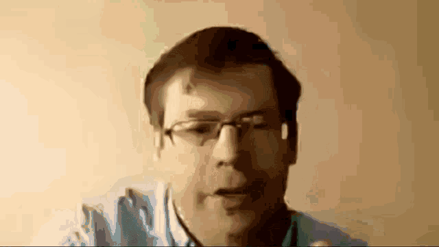 a man wearing glasses and a blue shirt is looking at the camera with his mouth open .