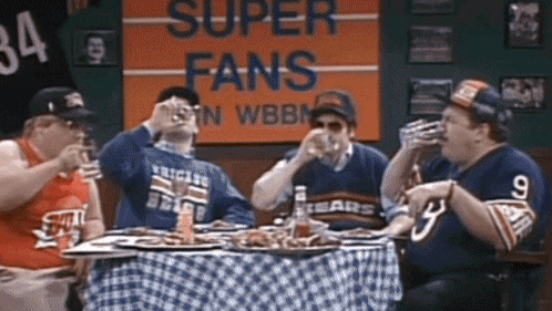 a group of men sit at a table drinking beer in front of a sign that says super fans in wbbm