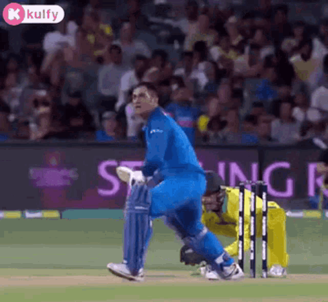 a man in a blue uniform is standing on a cricket field next to a wicket .