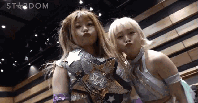 two women are posing for a picture and one has a belt that says ' stardom '