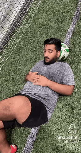 a man is laying on the grass with a soccer ball in his head .