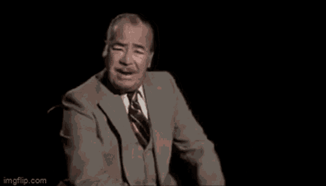 a man in a suit and tie is sitting in a chair with his eyes closed and says `` let 'em crash '' .