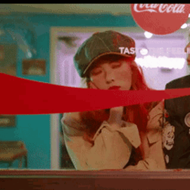 a woman in a hat is standing in front of a coca cola sign .