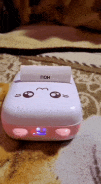a pink and white printer is sitting on a bed with a piece of paper on top of it .