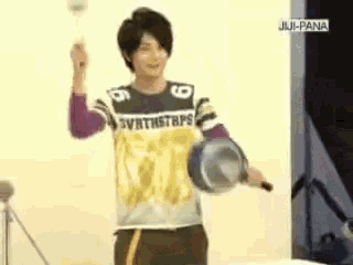 a man wearing a shirt that says synthstraps is holding a frying pan in his hand .