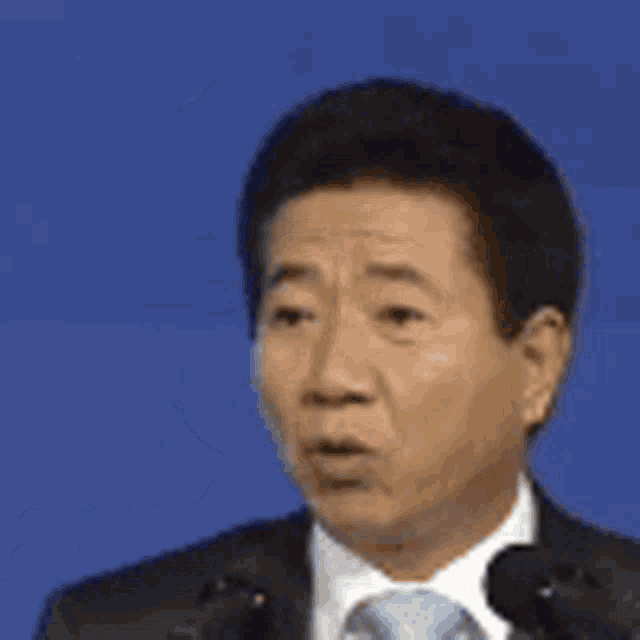 a man in a suit and tie is giving a speech in front of microphones .