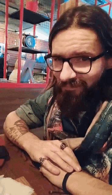 a man with glasses and a beard is sitting at a table with his hands folded