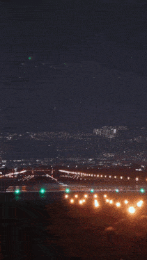 an airplane is taking off from a runway at night with a city in the background