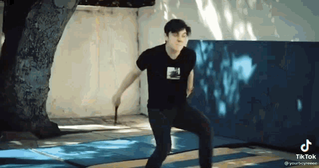a man in a black shirt is holding a stick in his hand while standing on a mat .