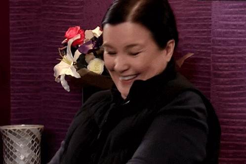 a woman sitting in front of a vase of flowers smiling