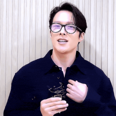 a man wearing glasses and a blue jacket is holding something in his hand