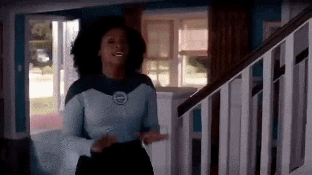 a woman is standing in a living room next to a staircase and a window .