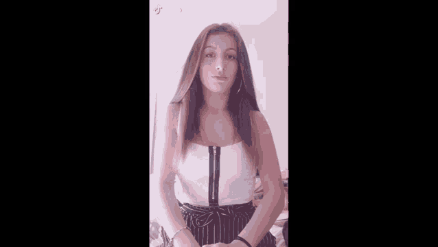 a woman wearing a white crop top and black striped pants is making a funny face .
