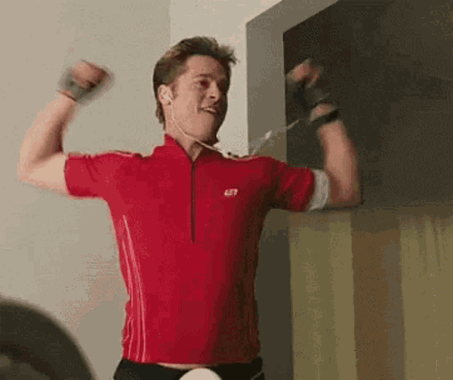 a man in a red shirt is flexing his muscles while wearing headphones and listening to music .