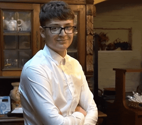 a young man wearing glasses and a white shirt is standing in front of a cabinet with the letter p on it