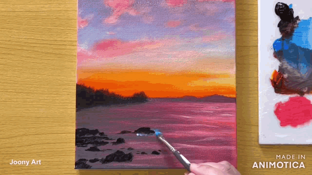 a painting of a sunset is being painted on a canvas by joony art