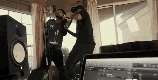 two men are singing into microphones in a living room with a laptop in the foreground .