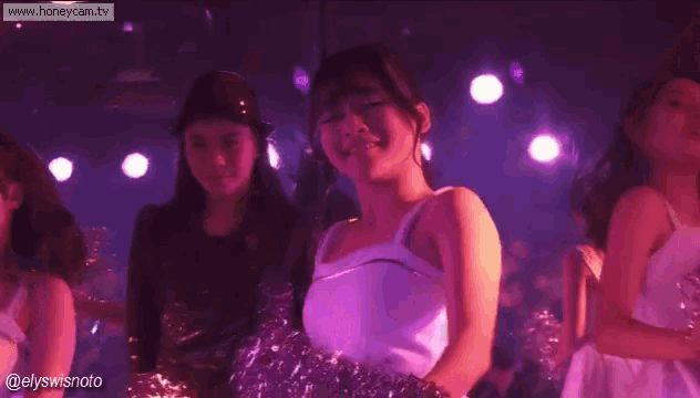 a group of women in white dresses are dancing on a stage in a dark room .