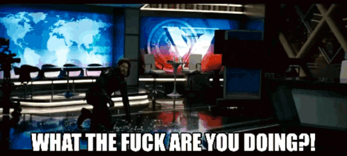 a man in a black suit is standing in front of a large screen that says ' what the fuck are you doing ? '