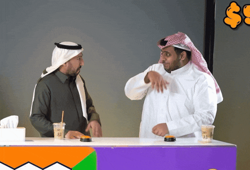 two men are standing behind a counter with a purple sign that says ' s ' on it