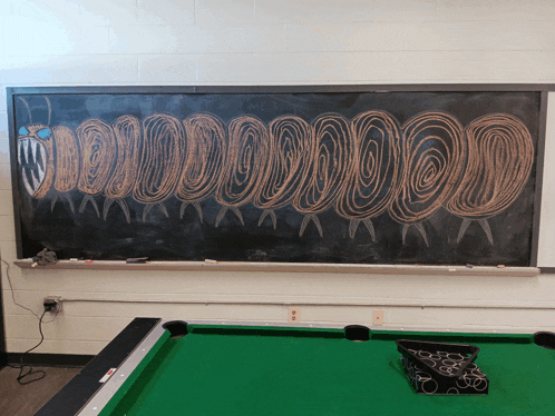 a pool table in front of a chalkboard with a drawing of a caterpillar on it