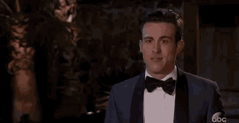 a man in a tuxedo and bow tie is holding his fist up in the air .