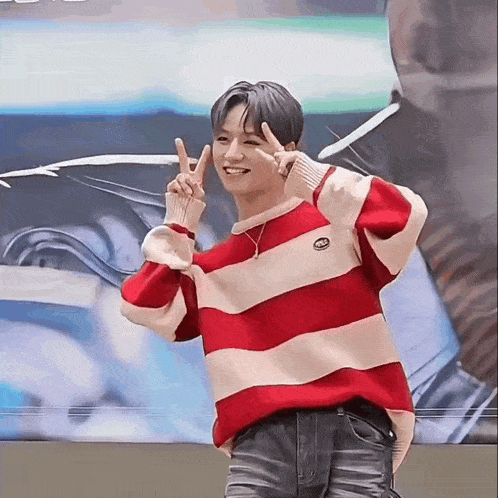 a young man wearing a red and white striped sweater is giving the peace sign .