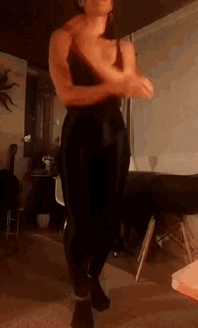 a woman in a black tank top and black pants is standing in a living room .