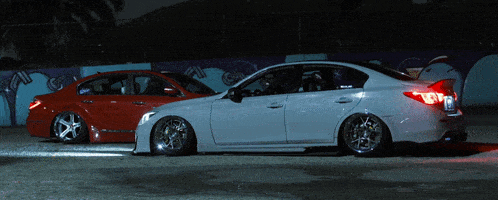 a red car is parked next to a white car in front of a graffiti wall