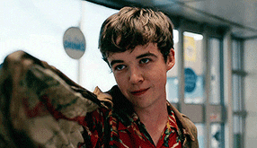 a young man is standing in front of a bus stop holding a blanket .