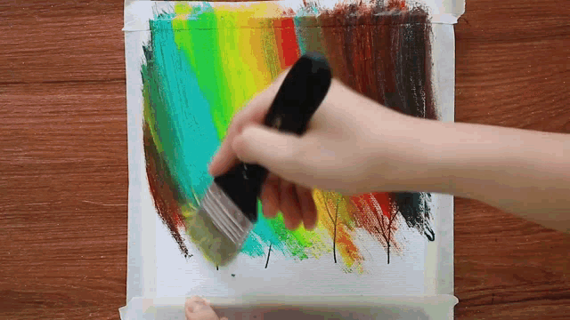 a person is painting a rainbow with a brush on a piece of paper