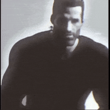 a man with a beard wearing a black shirt is standing in the dark
