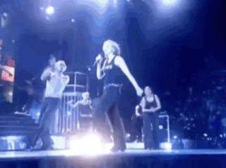 a woman is singing into a microphone on a stage in front of a crowd of people .