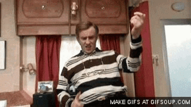 a man in a striped sweater is dancing in a room in a trailer .