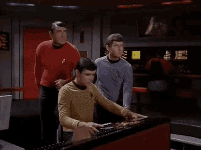 a man in a yellow shirt with a star trek logo on his chest is using a computer