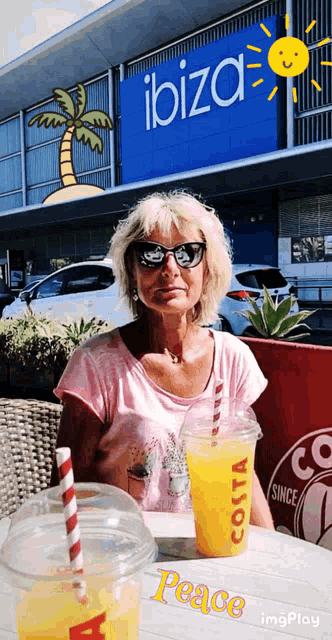 a woman sits at a table with two cups of orange juice in front of a ibiza store