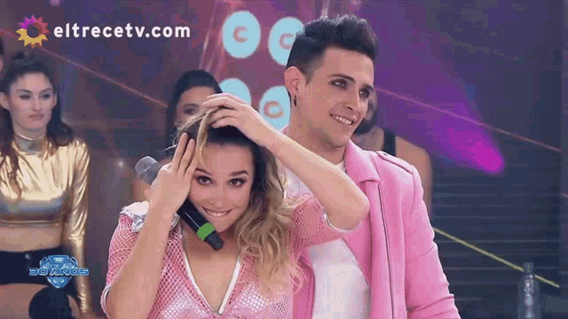 a man in a pink jacket holds a woman 's hair in front of a eltrecetv.com banner