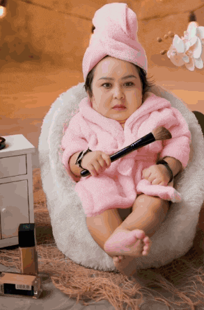a baby with a towel wrapped around her head holds a makeup brush