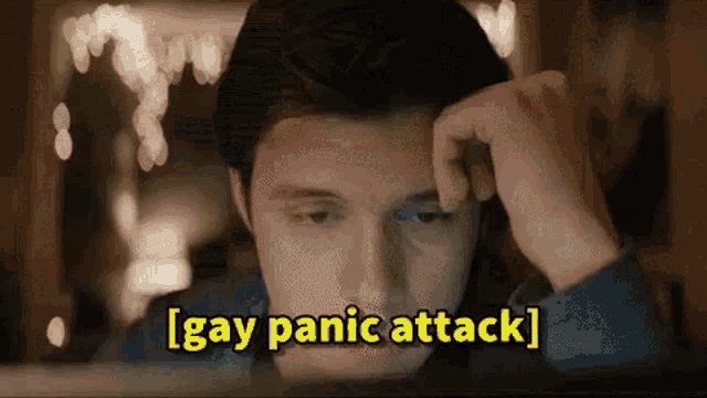 a man is sitting in front of a computer screen with his hand on his head and the words `` gay panic attack '' written above him .