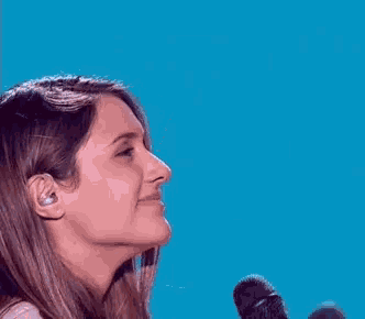 a woman is smiling while talking into a microphone against a blue background .