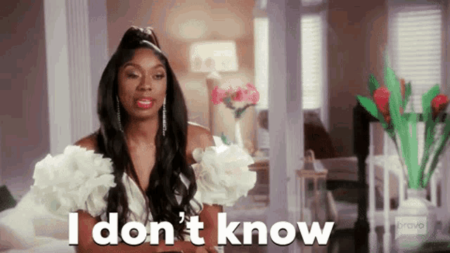 a woman in a white dress is standing in a living room and says `` i don 't know '' .