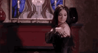 a woman in a black dress is dancing in a room with candles and a painting on the wall .